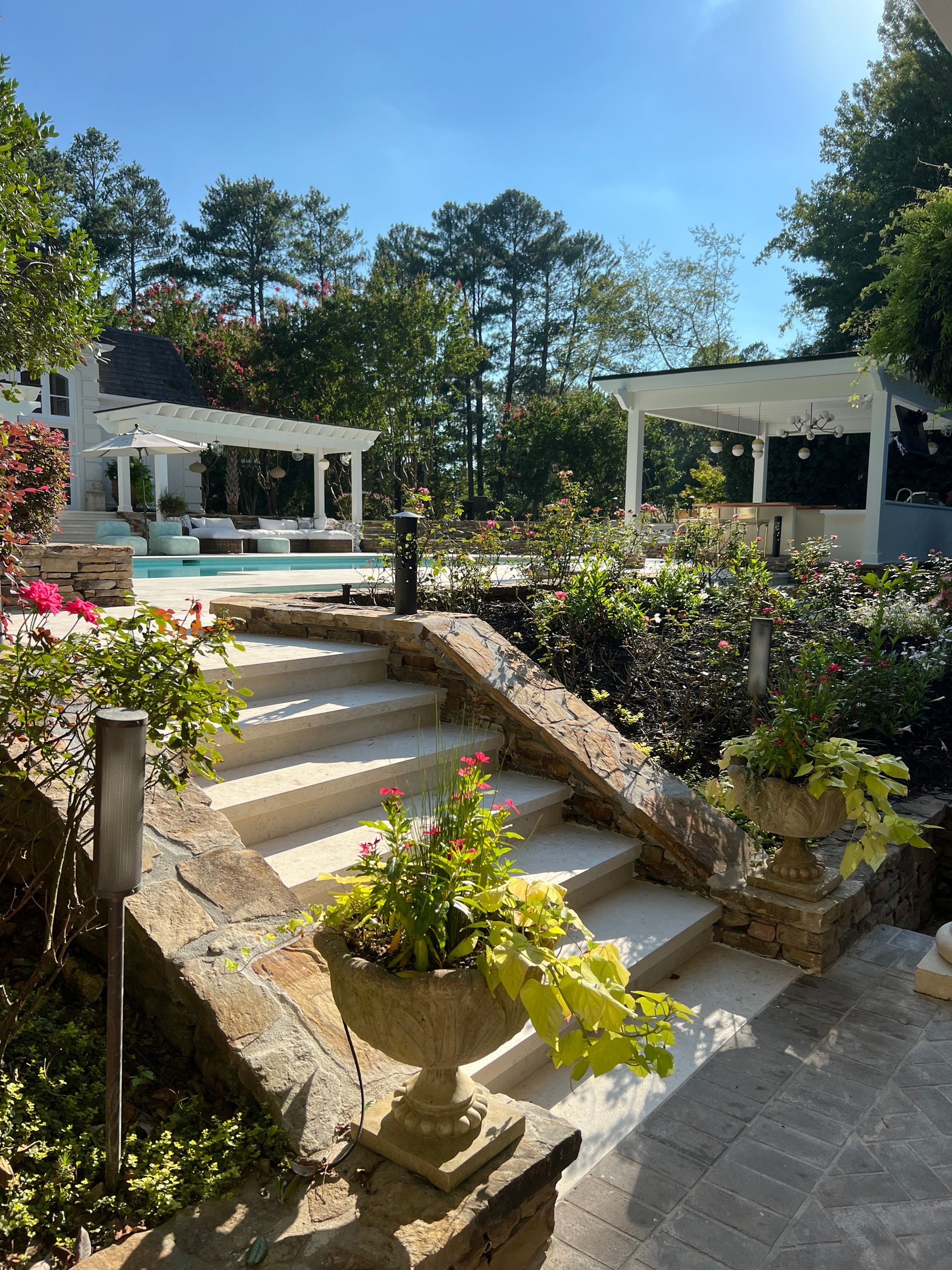 A garden with stairs leading up to a pool and a pergola.