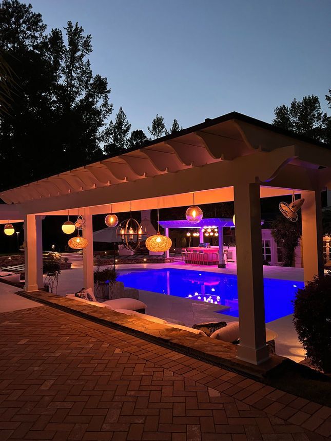 A large swimming pool is under a pergola at night