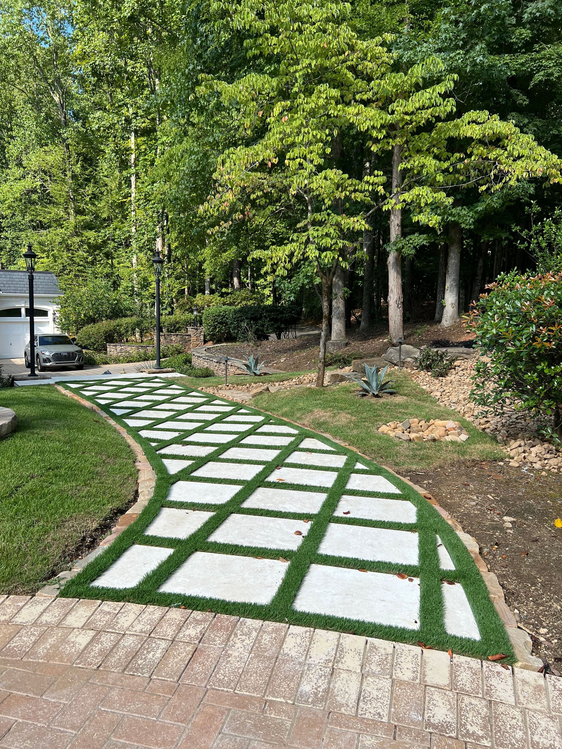 A brick walkway surrounded by grass and trees in a yard.