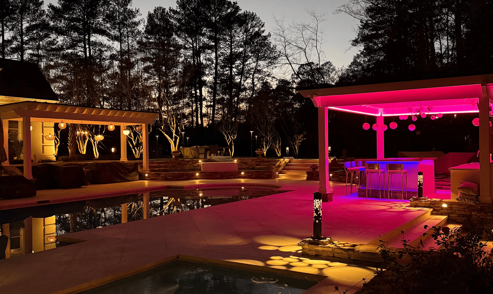 A patio area with a pool and a gazebo lit up at night.