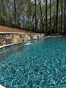 A large swimming pool surrounded by trees and a stone wall.
