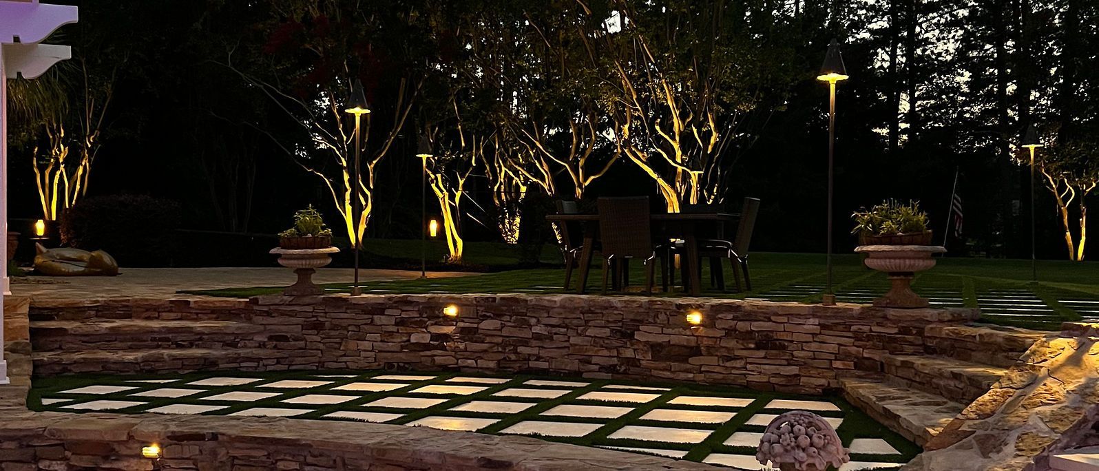 A patio with a stone wall and trees lit up at night.