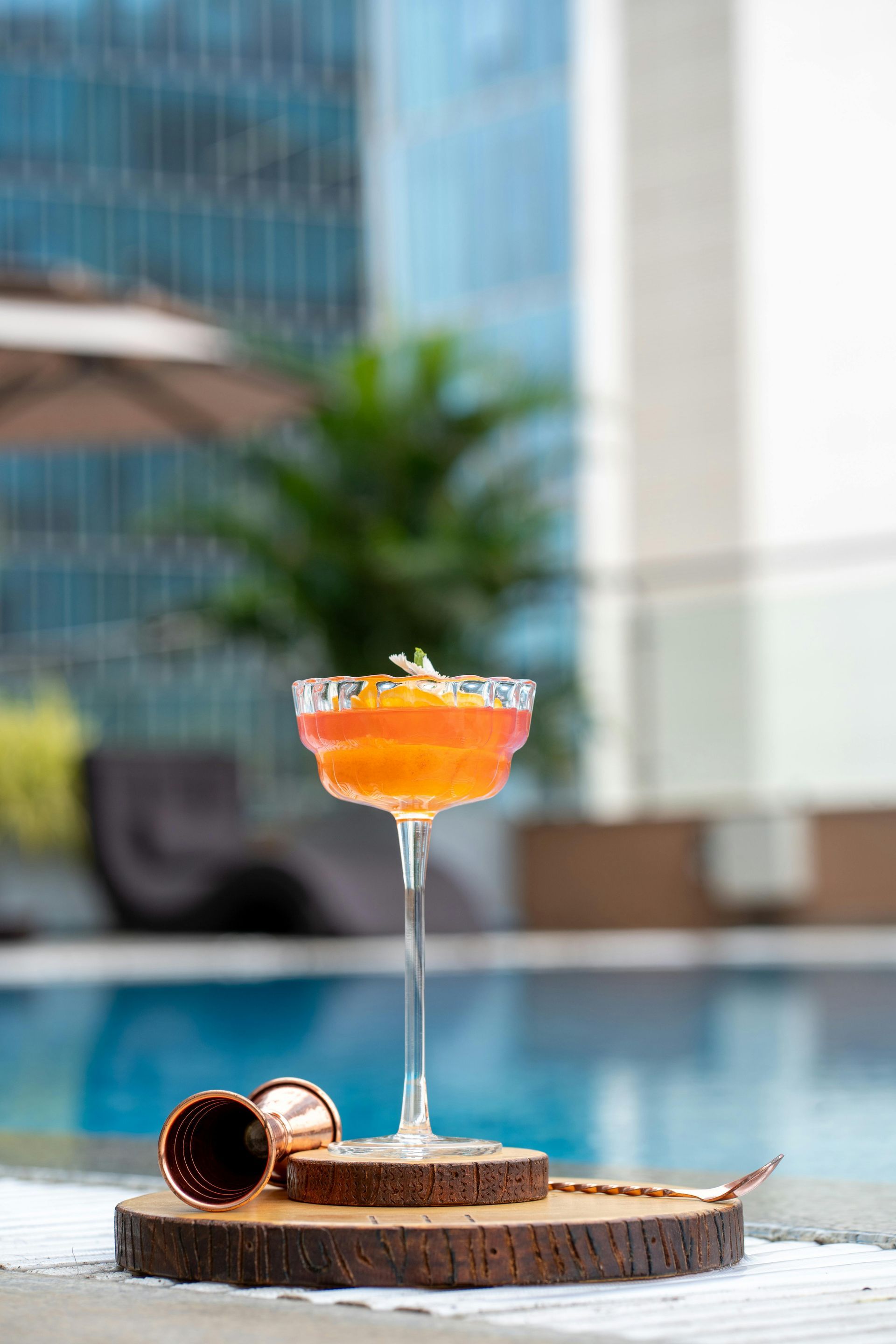 A cocktail is sitting on a wooden cutting board next to a swimming pool.