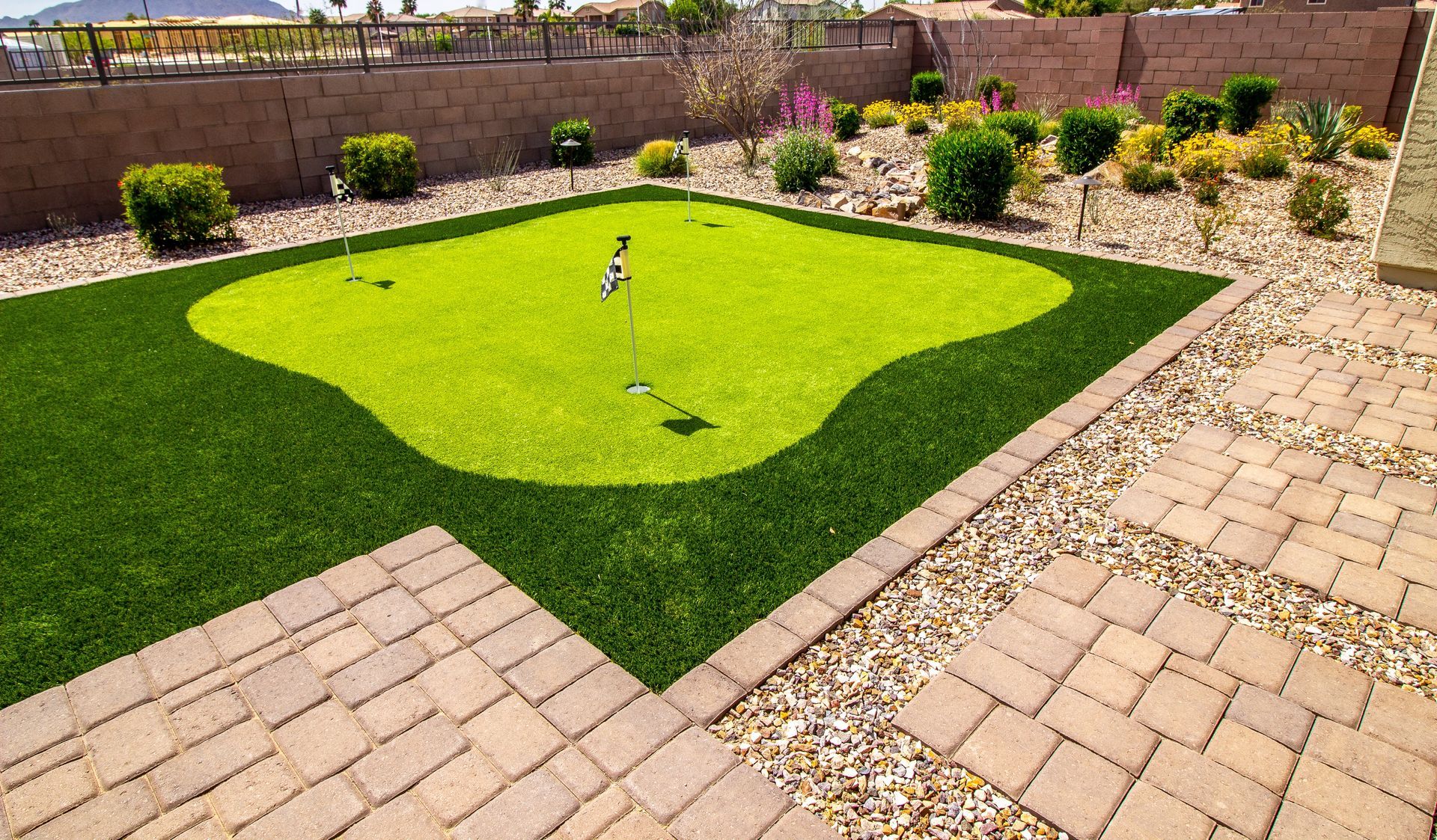 A backyard with a putting green and a brick walkway.