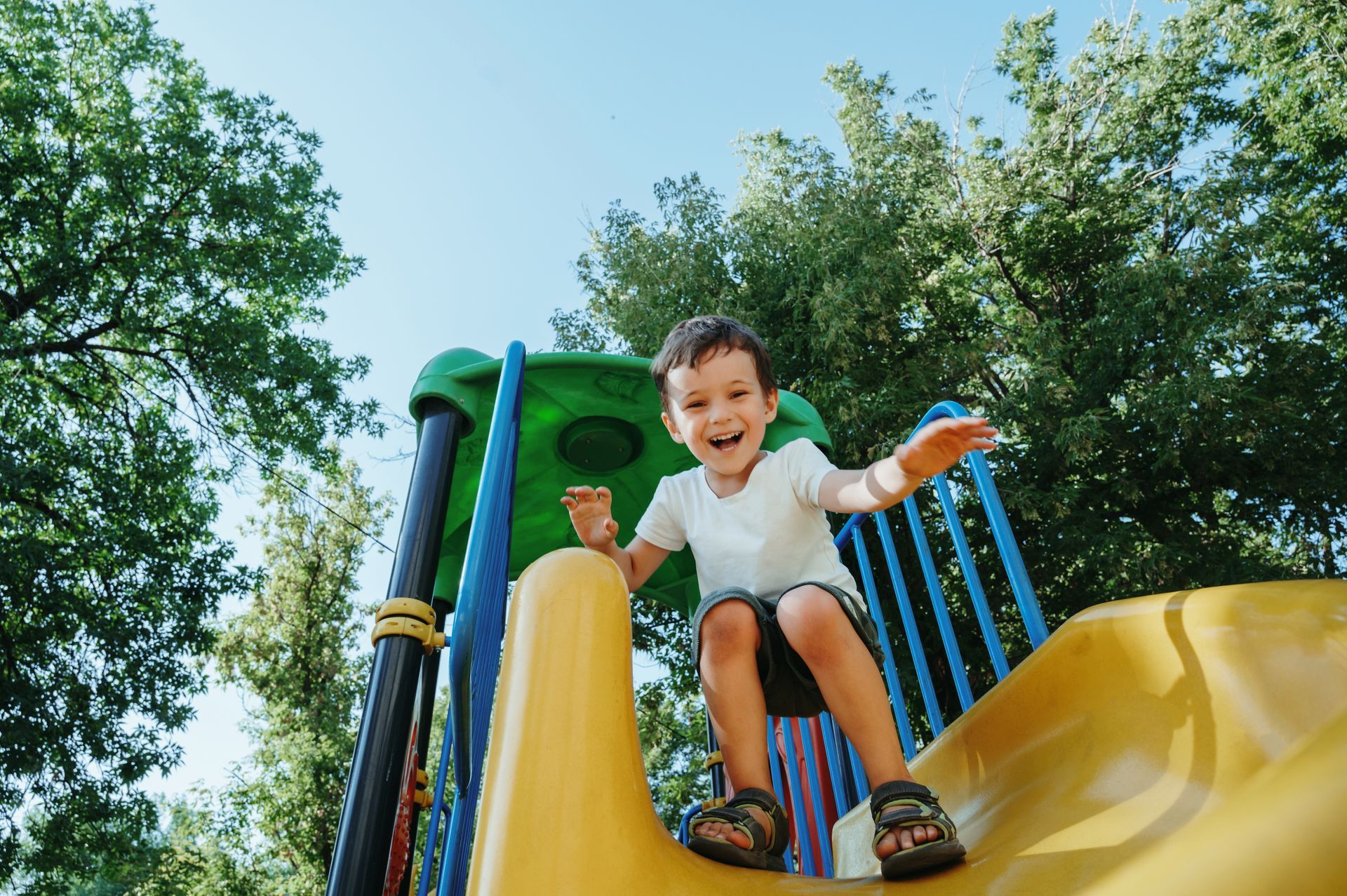 A young boy is sitting on a yellow slide at a playground.