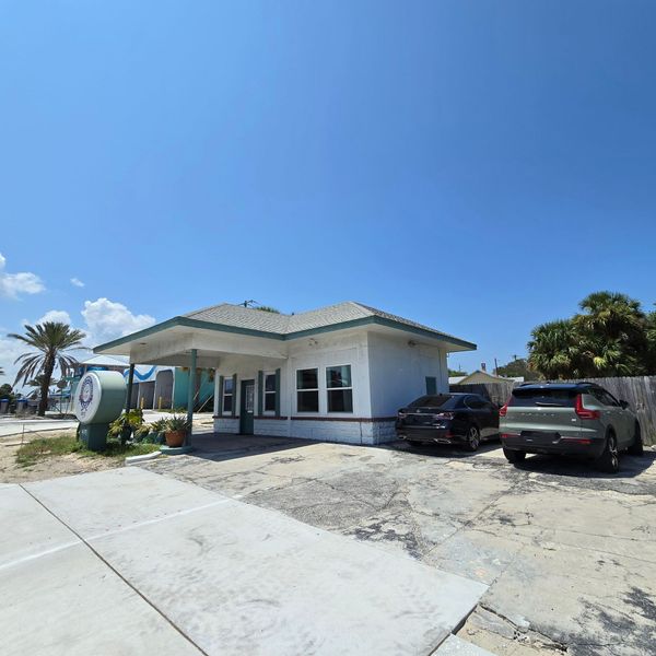 Two cars are parked in front of a small white building