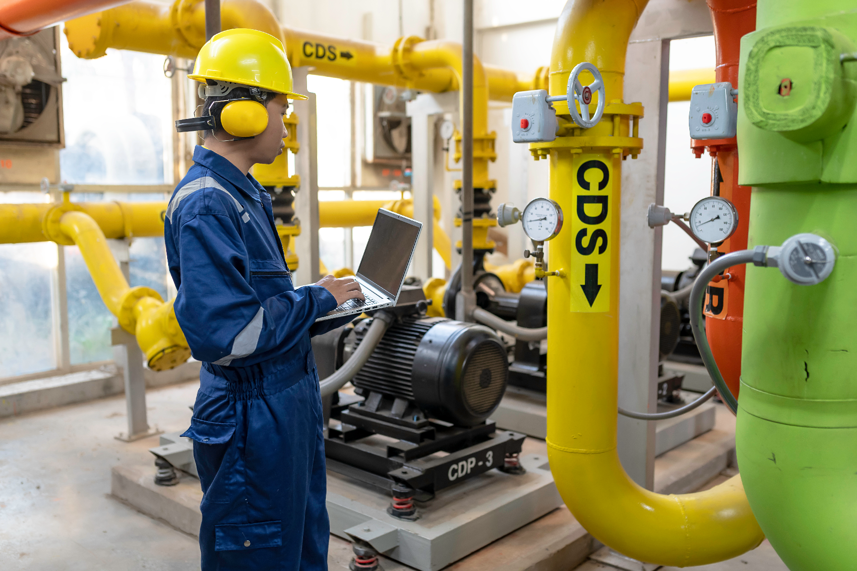 A man wearing a hard hat and ear muffs is working on a machine in a factory.