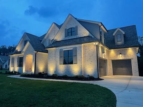 A large white brick house with a garage is lit up at night.