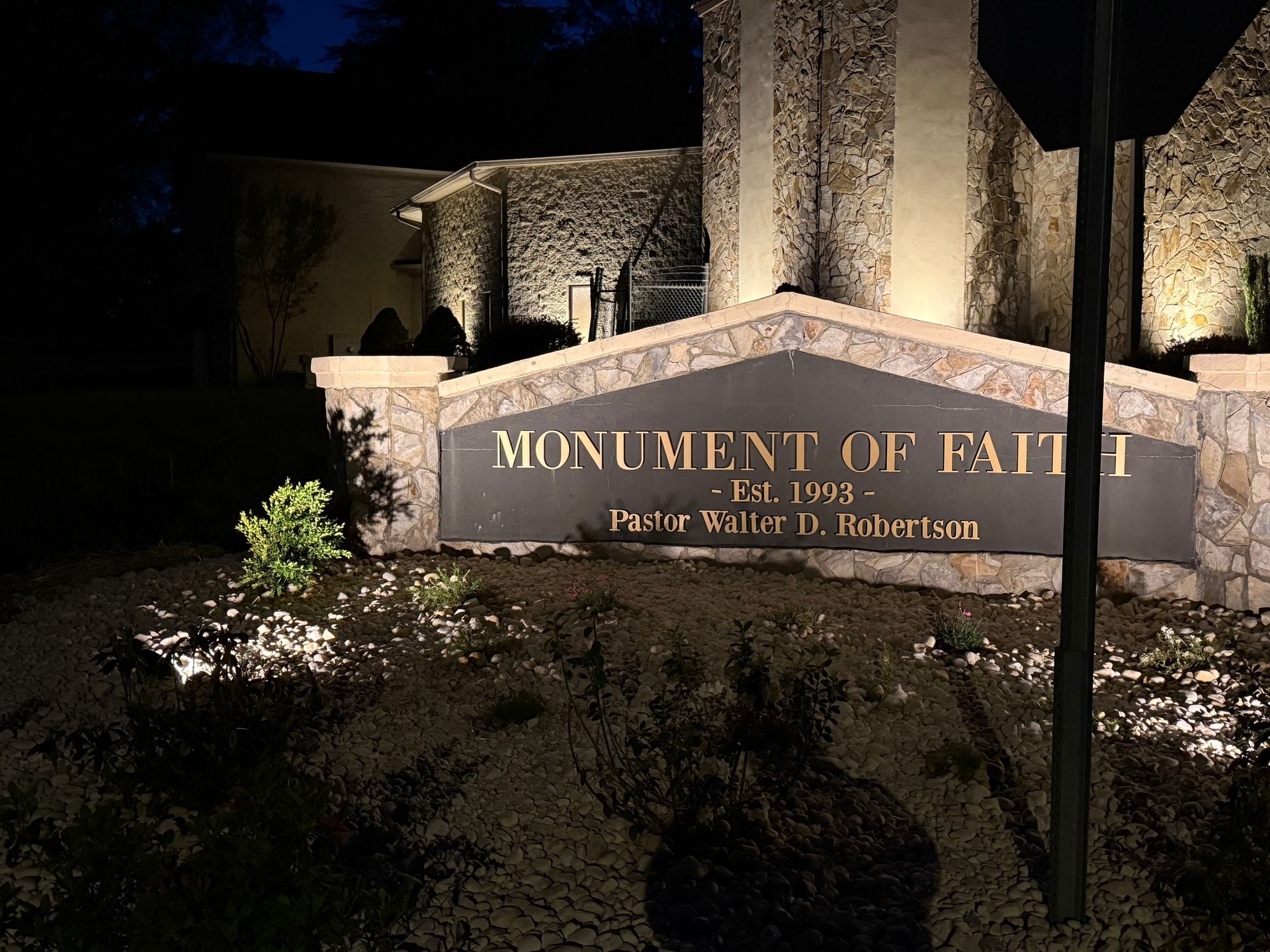Monument of Faith sign with illuminated text, set against a building facade at night.