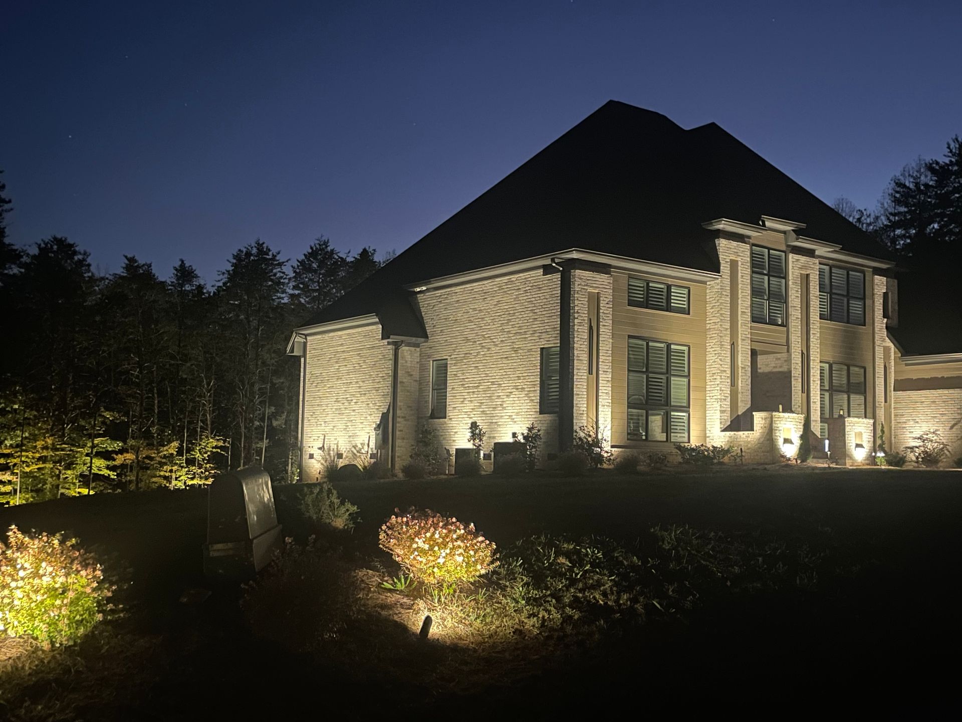 A large house is lit up at night with landscape lighting