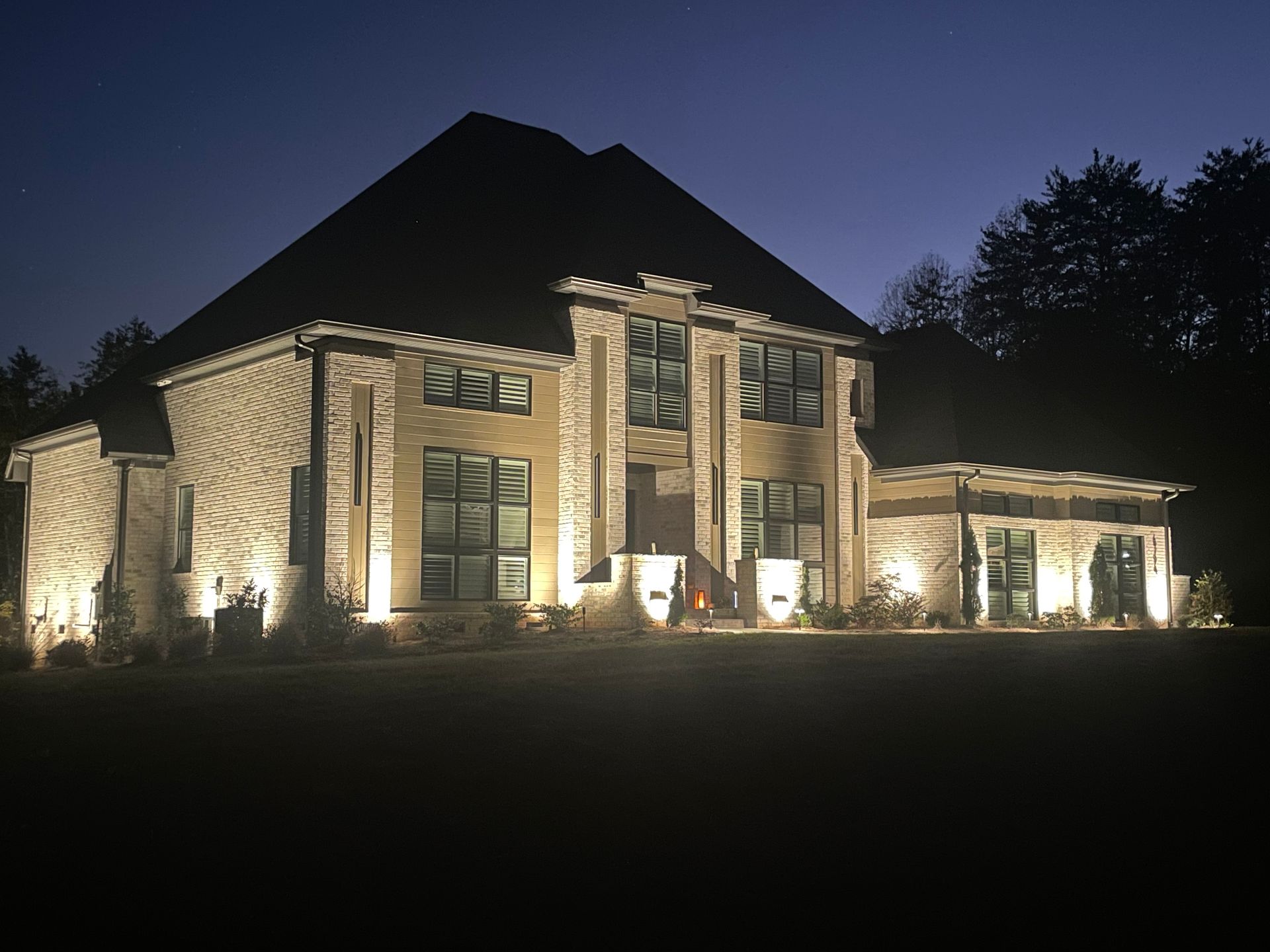 A large brick house is glowing with architectural lighting