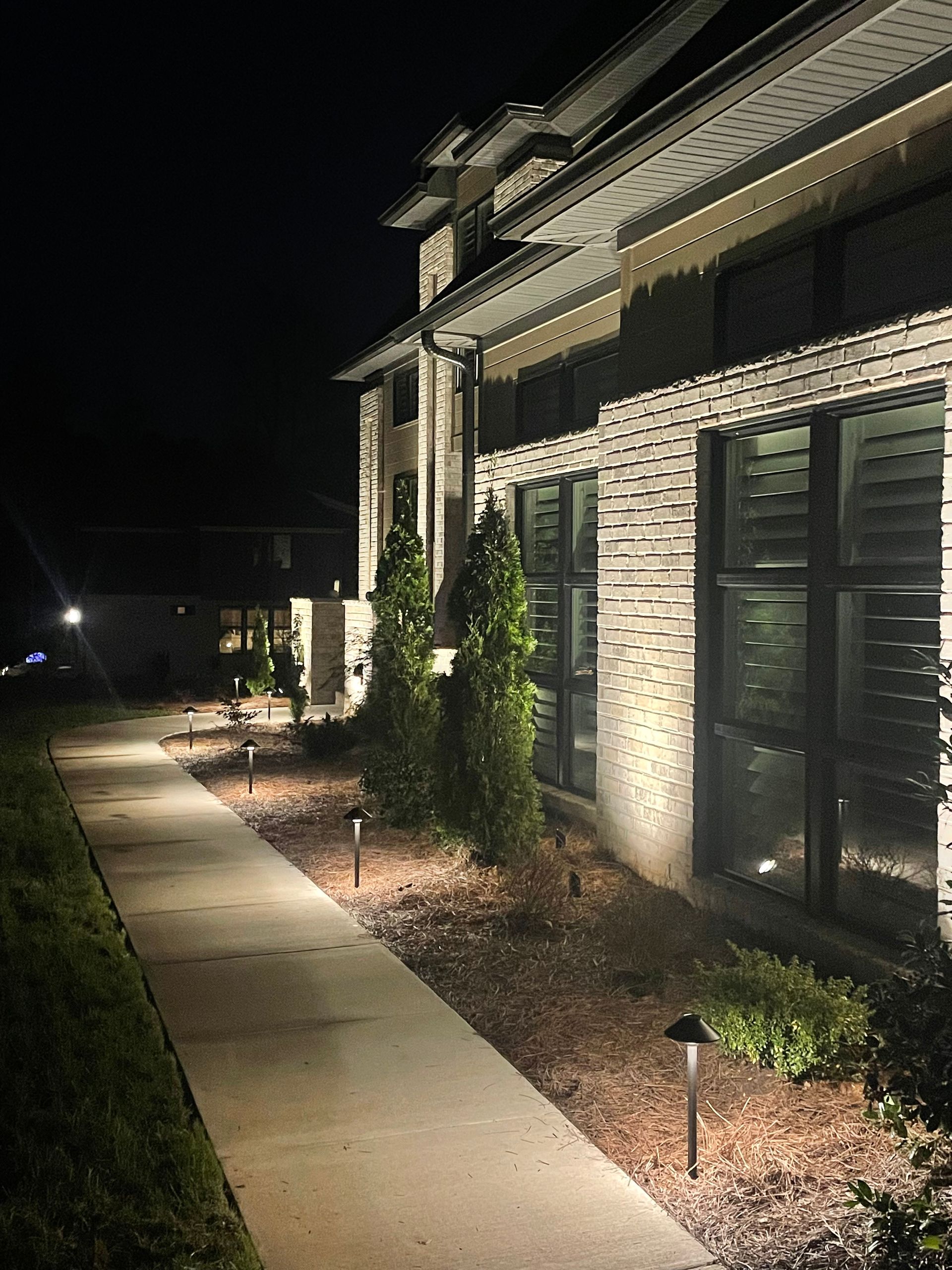 sidewalk along a brick home with elegant exterior lighting lamps.