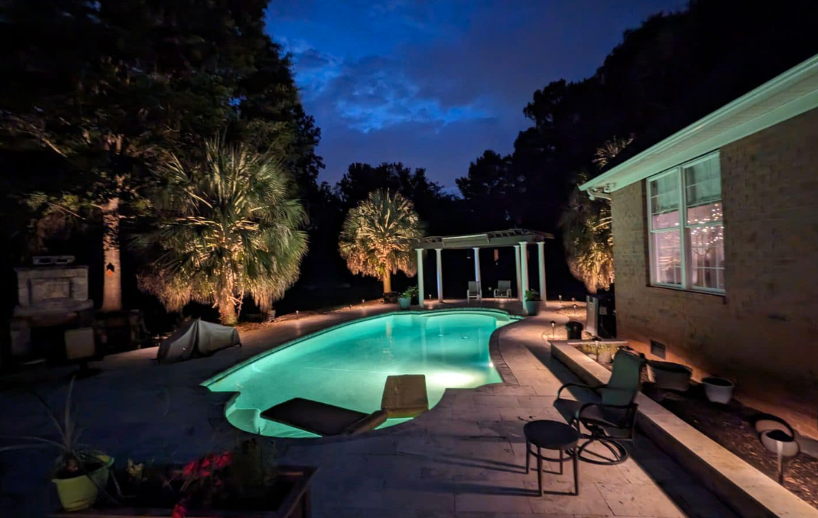 A large swimming pool is lit up at night in a backyard.