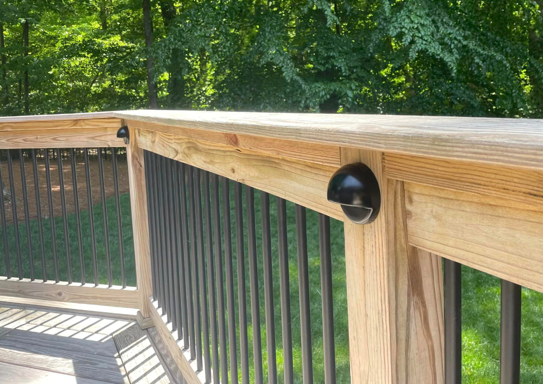 A wooden deck with a black lights installed, and trees in the background.