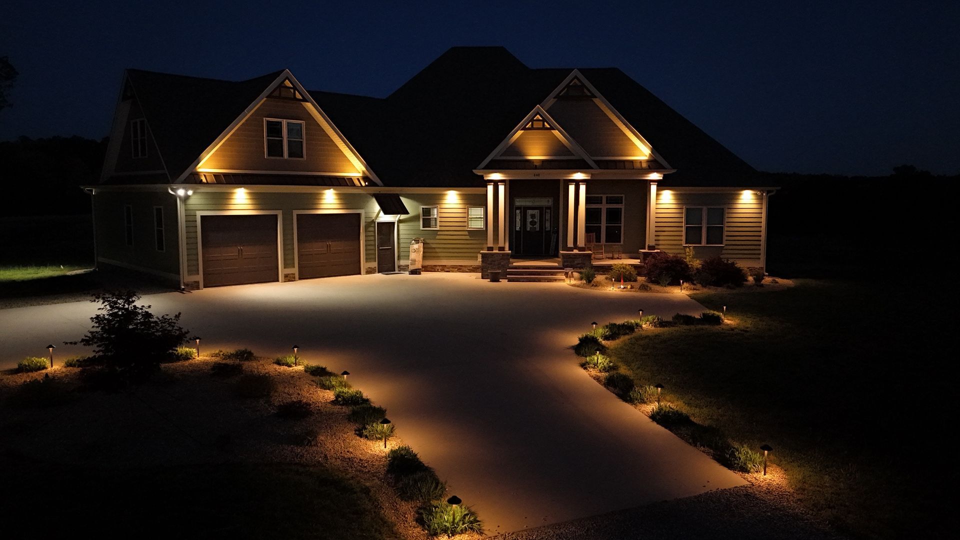 House exterior illuminated with warm lights at night, driveway and landscaping.