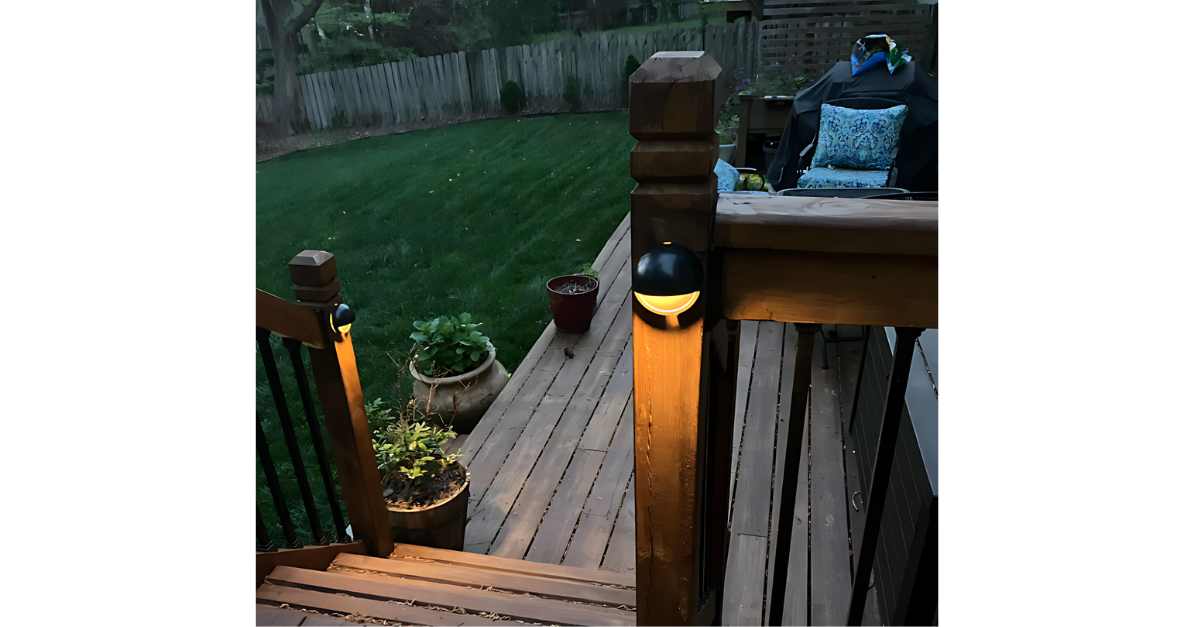 A wooden deck with stairs and a light on the railing at night.