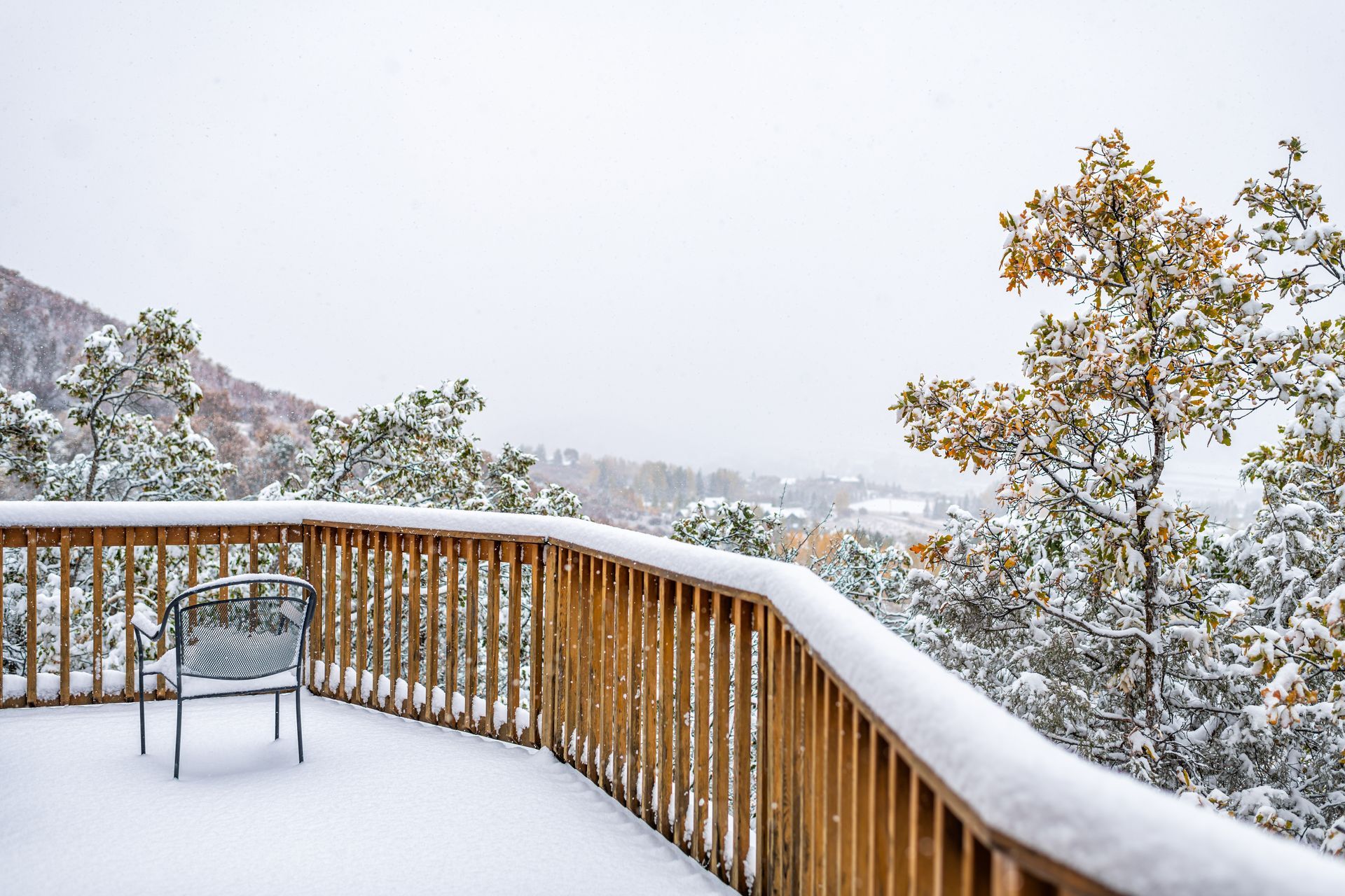 A snowy deck in a residential backyard, overlooking a picturesque nature view with hills and trees