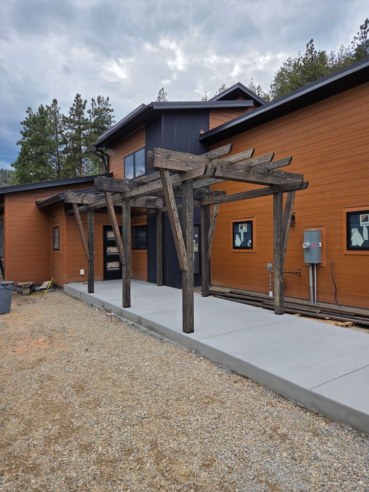 Brick building with pergola, gray walkway, and gravel pathway. Dark wood accents under cloudy sky.