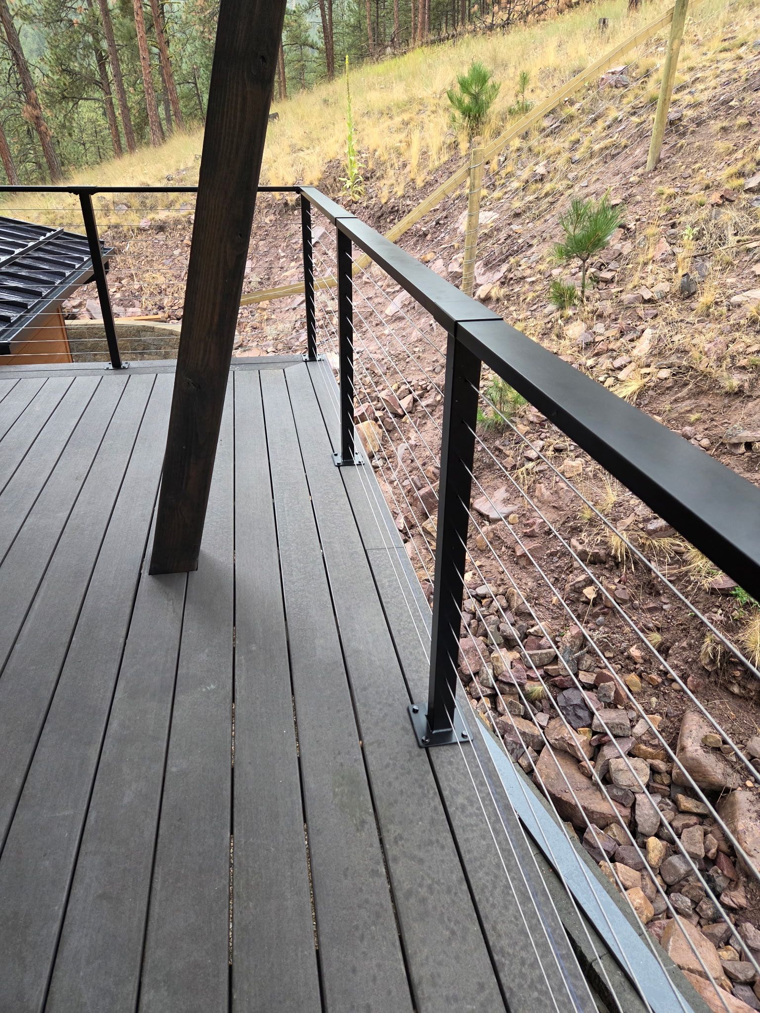 Deck with gray planks, black railing, and a wooded hillside in the background.