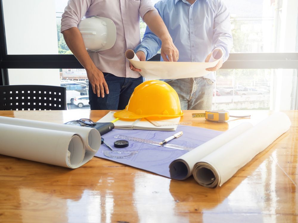 Two architects reviewing blueprints at a desk, with safety helmets and tools visible.