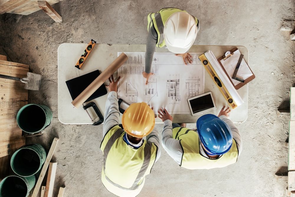 Construction workers in hard hats and vests reviewing blueprints at a table.