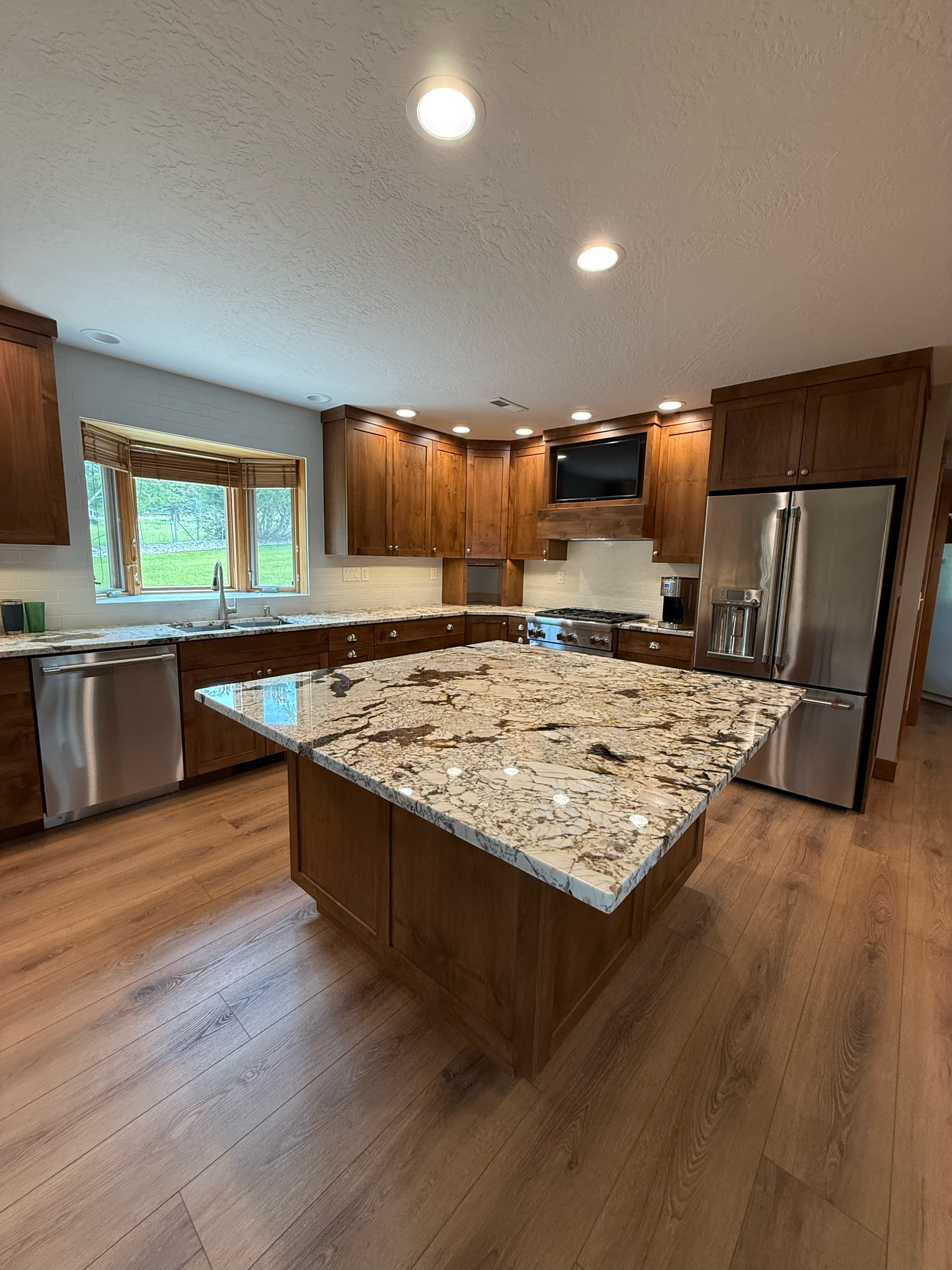 Modern kitchen with wood cabinets, granite island, stainless steel appliances, and recessed lighting.