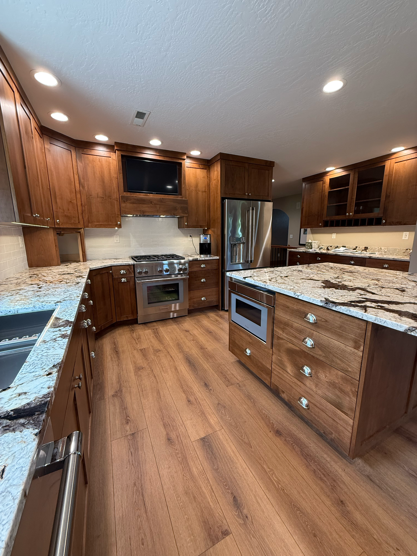 A kitchen with wood cabinets, granite countertops, stainless steel appliances, and wood-look flooring.