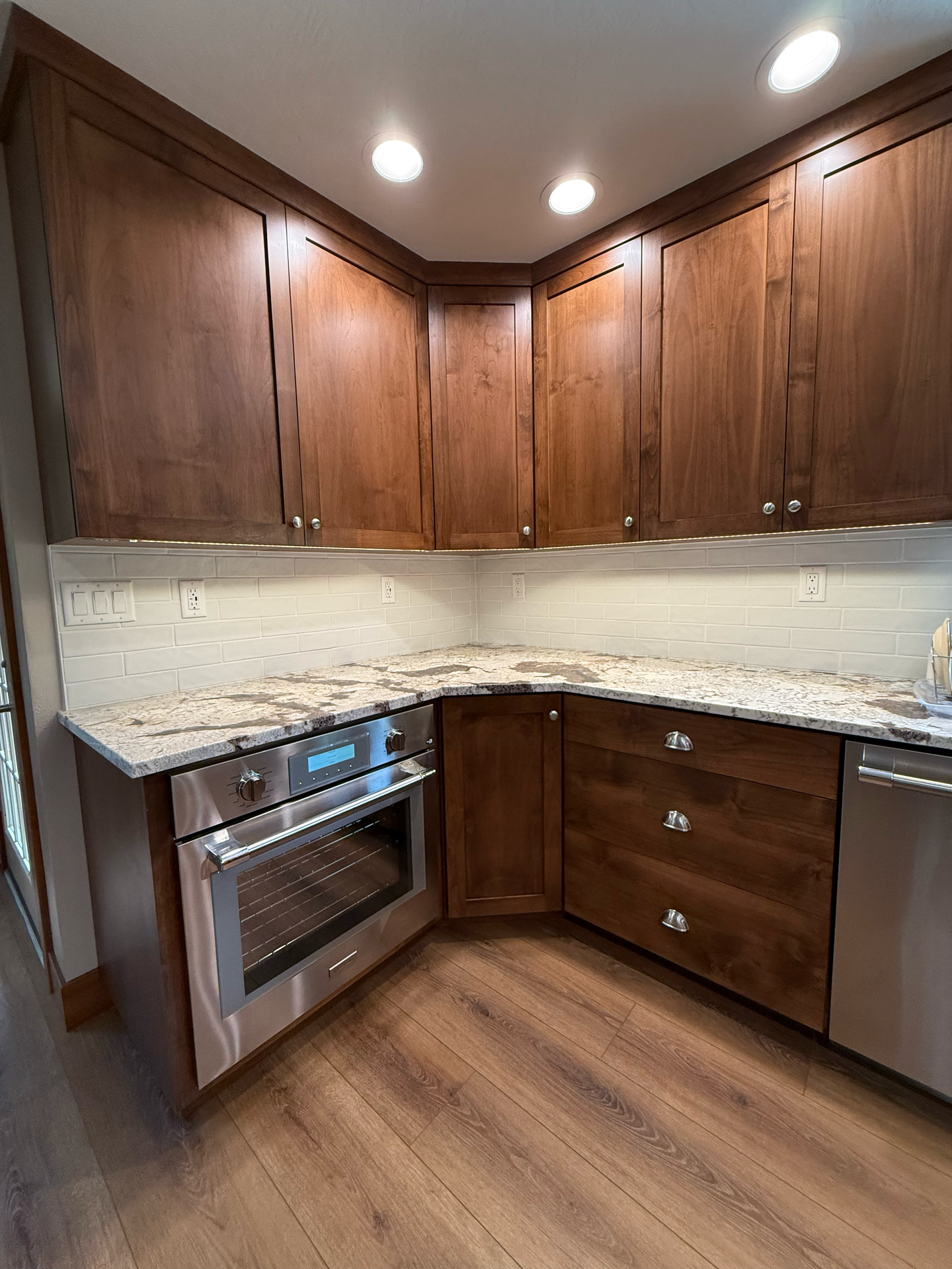 Kitchen corner with brown cabinets, stainless steel oven, and granite countertops.