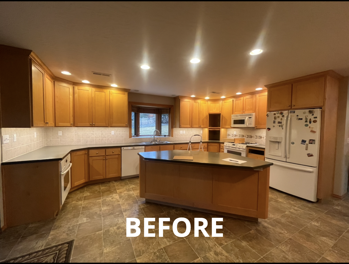 Before photo of a kitchen with light wooden cabinets, granite countertops, and a central island.