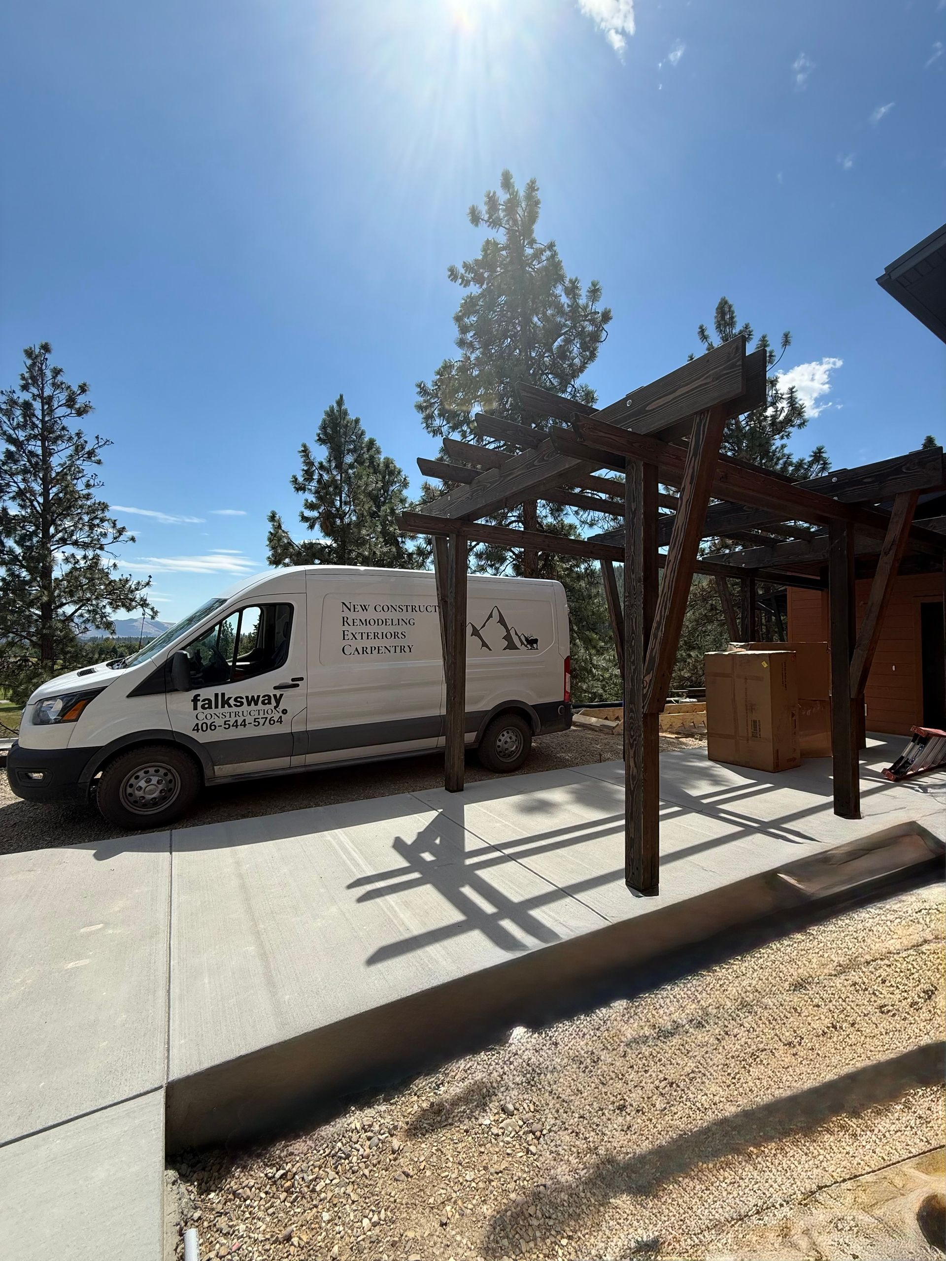 White van parked under a wooden pergola on a sunny day, with blue sky and trees in the background.