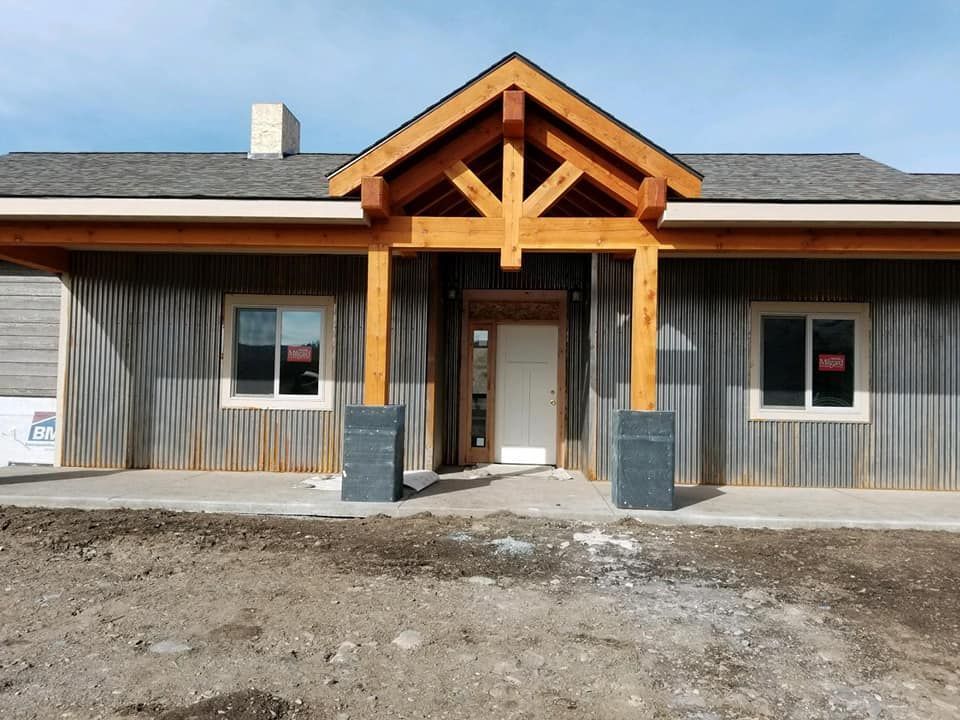 Front view of a house with wooden porch and gray siding. The doorway has a wooden truss.