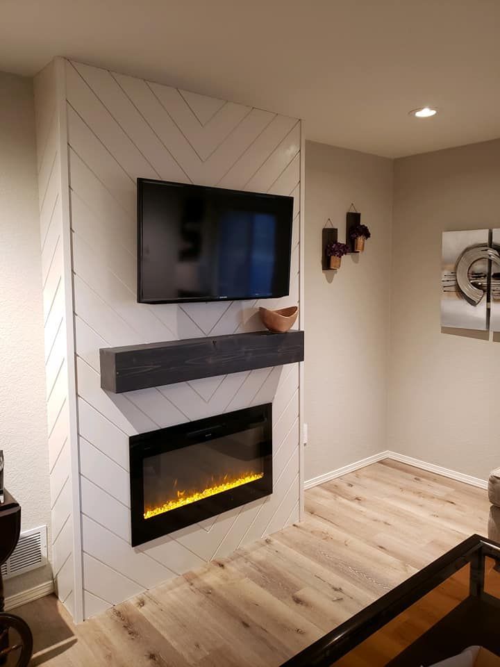Fireplace with TV and floating shelf on a white herringbone wall, wood floor.