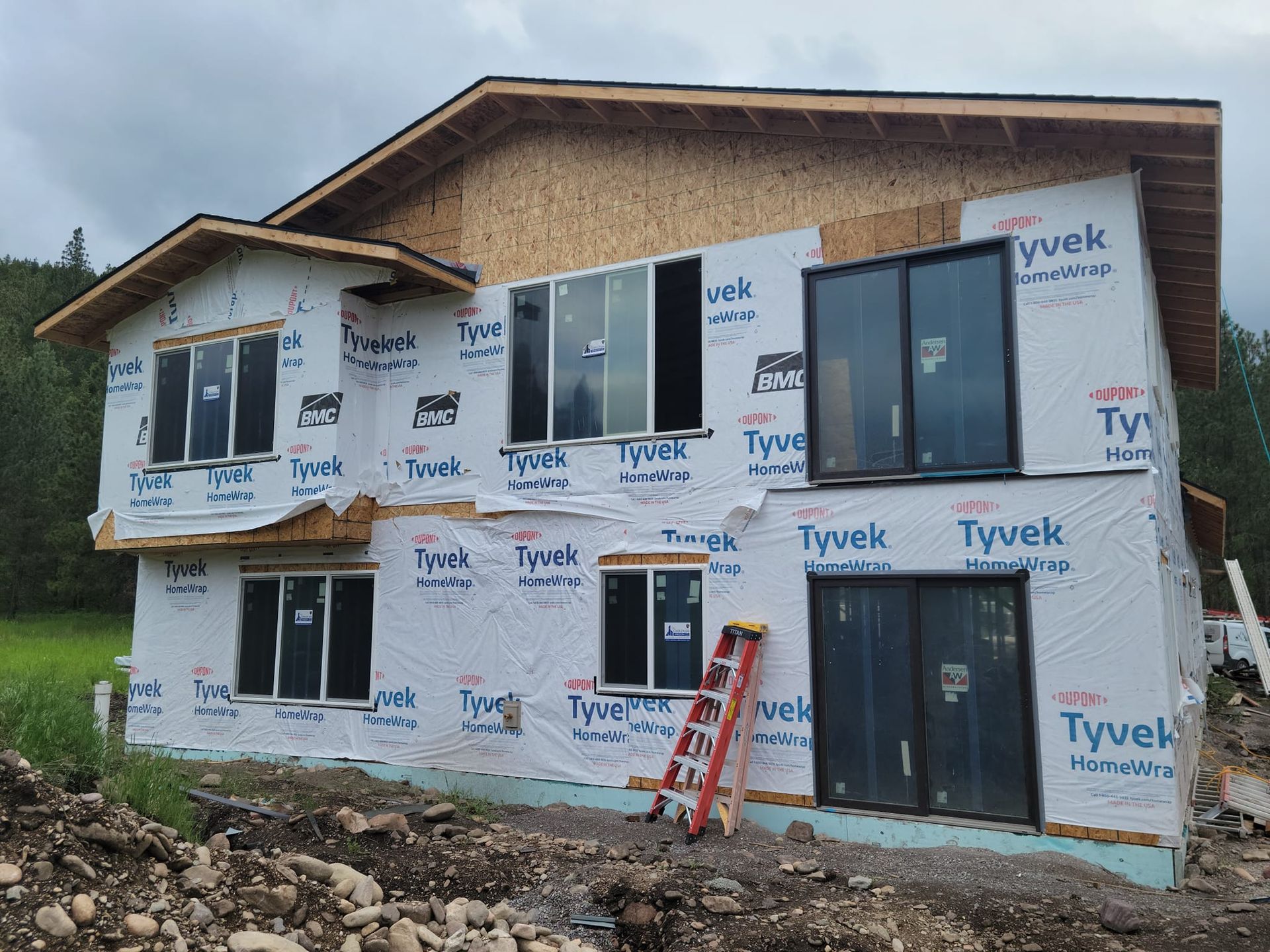 House under construction, wrapped in Tyvek, windows installed, and a ladder leaning against the side.
