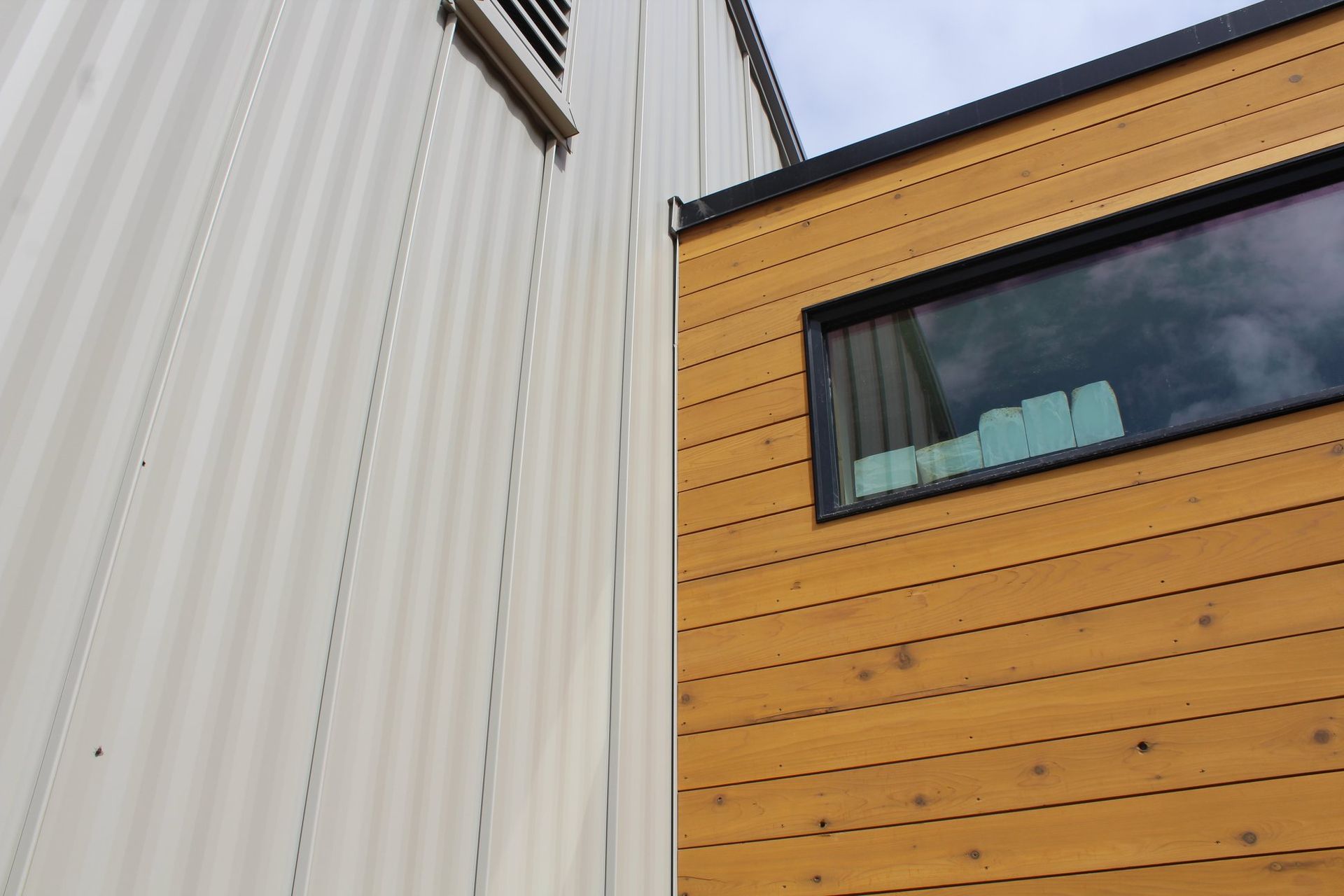 Exterior view of a building with a white corrugated metal wall and a wooden plank wall with a window.