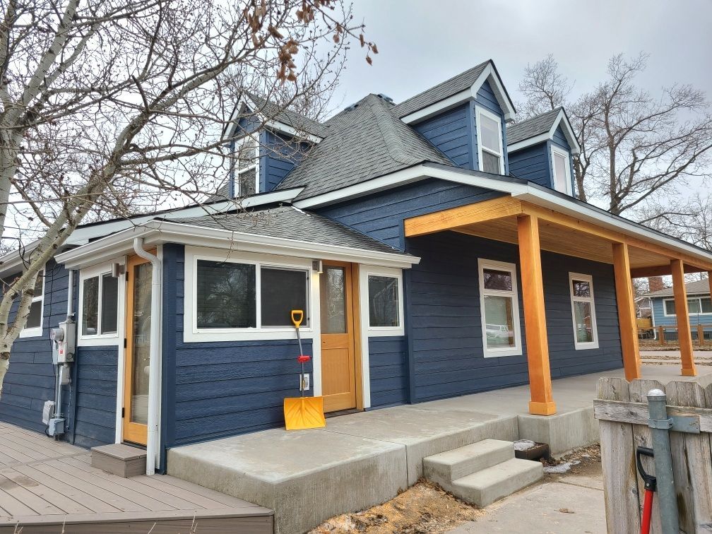 Blue house with wooden porch, stairs, and light tan trim. Two dormers on roof.