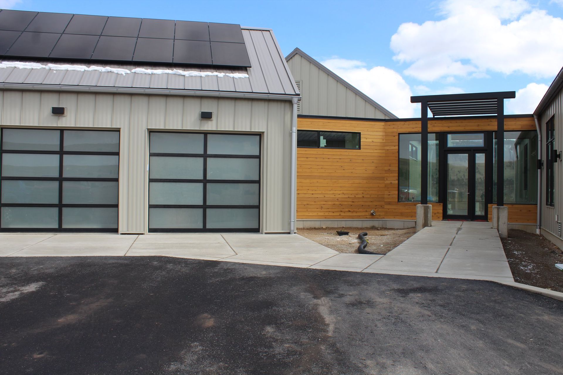 Modern home with garage and solar panels; wooden siding and pathway lead to entrance.