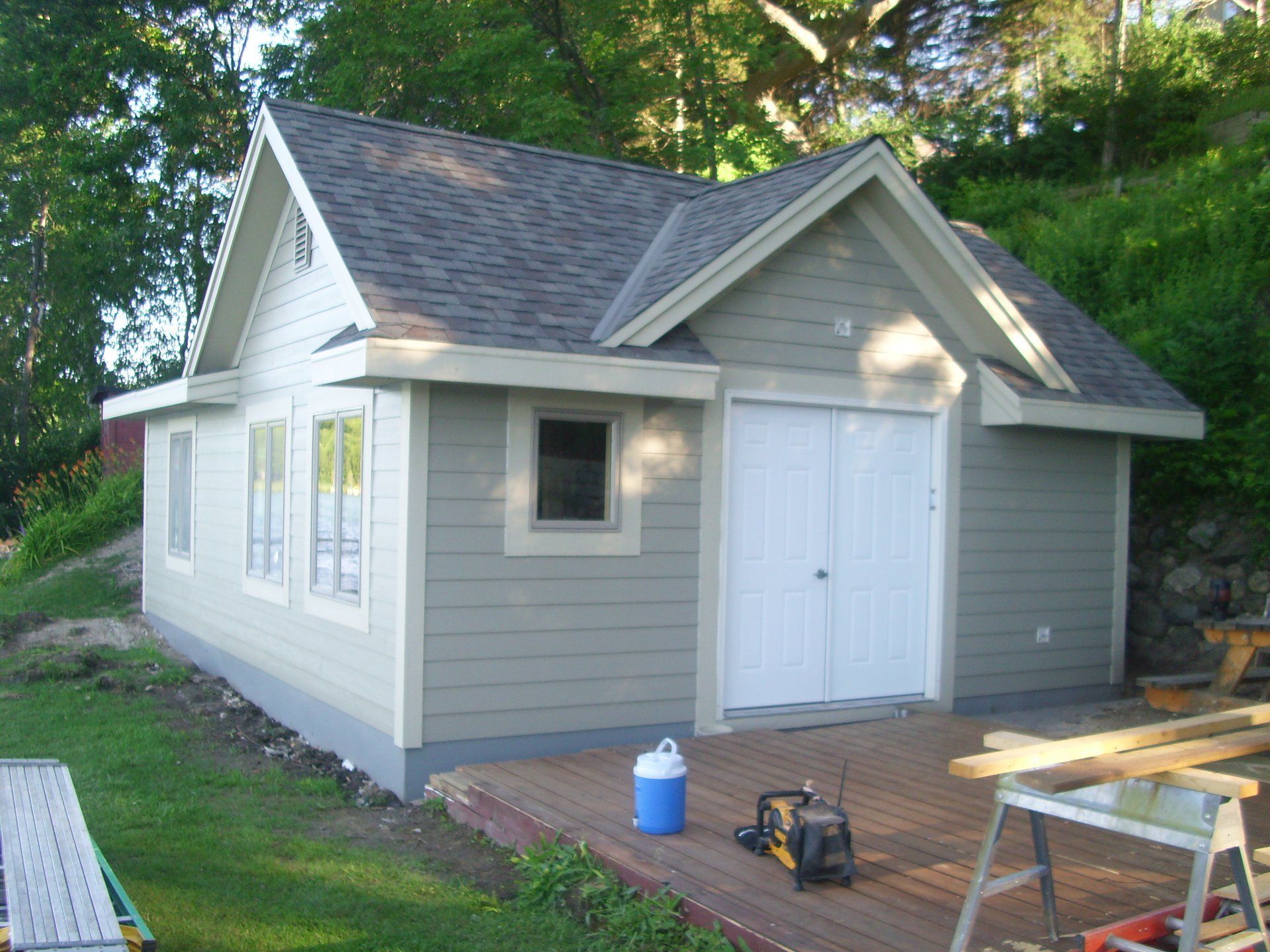 Small light green shed with white trim, double doors, and a grey roof.
