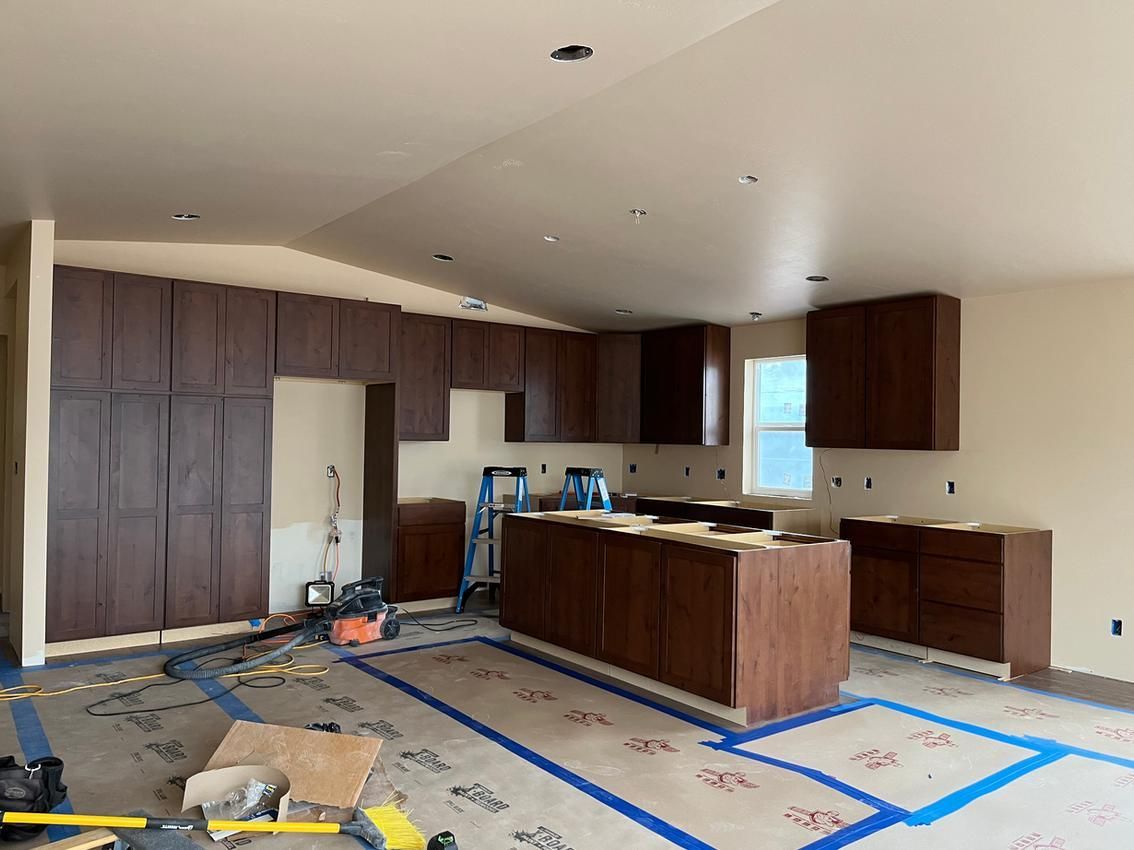 Kitchen cabinets under construction, dark brown against light walls. Blue tape on floor.