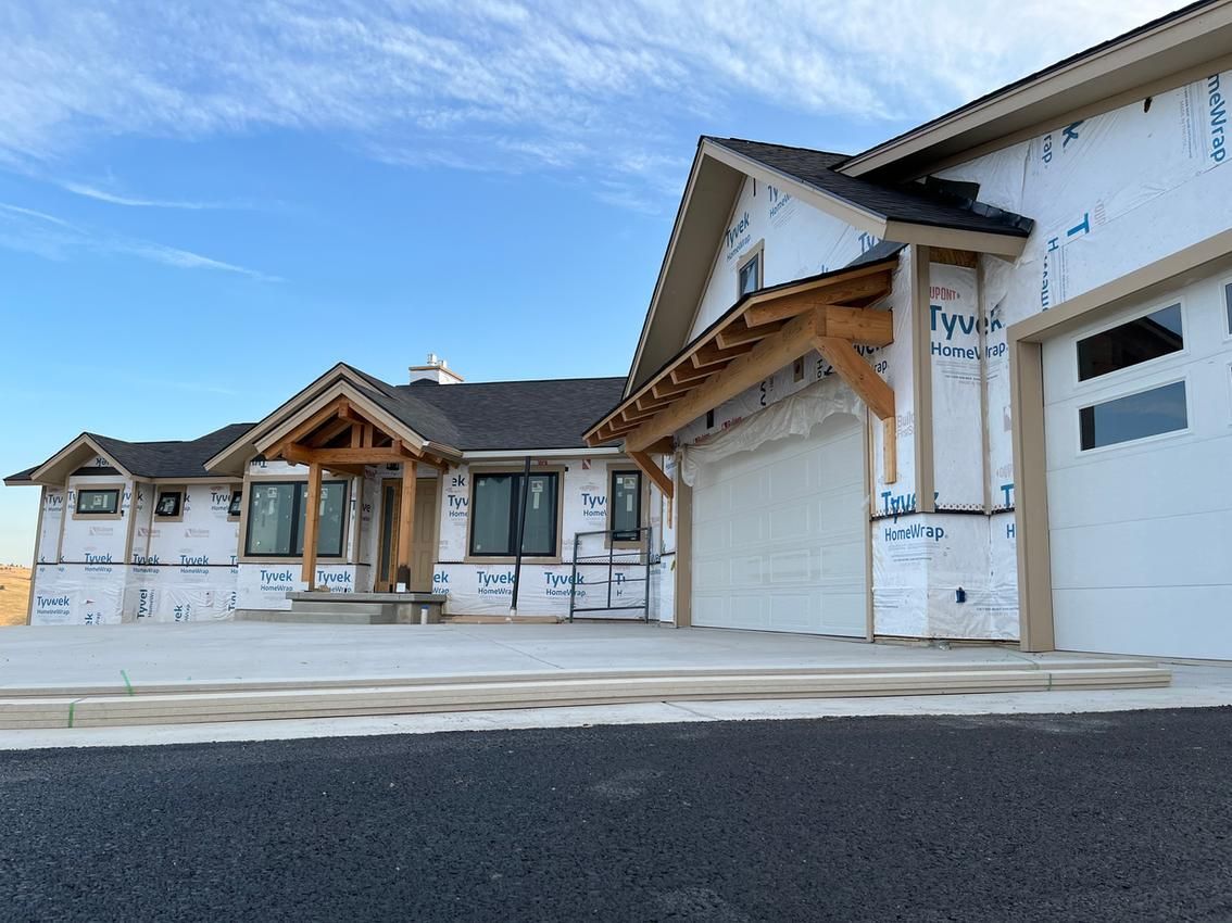 A house under construction wrapped in Tyvek, with exposed wood beams and a two-car garage.