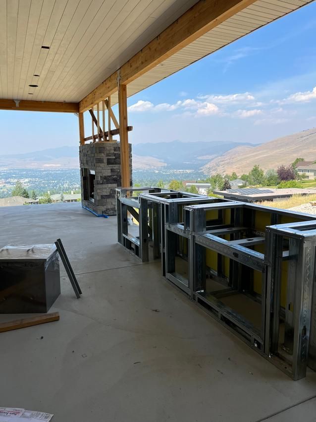 Outdoor kitchen under construction with mountain view. Steel frames, stone fireplace, concrete floor.