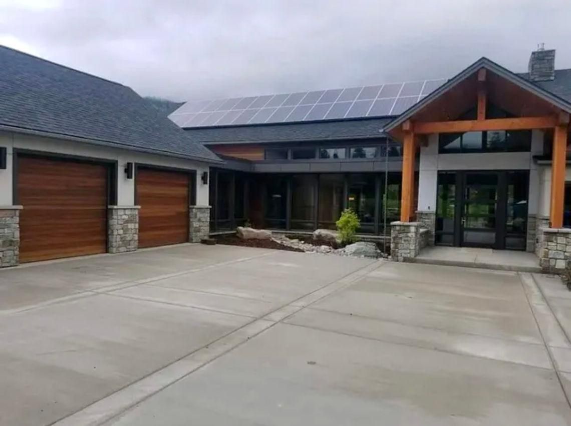A modern house with solar panels, wooden garage doors, and a concrete driveway.
