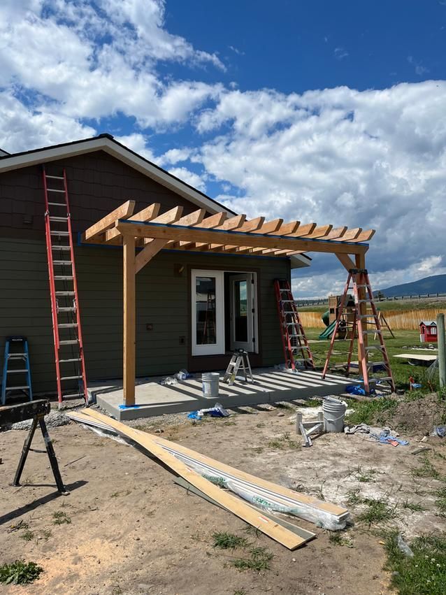 A pergola being built outside a house with ladders and building materials scattered around.