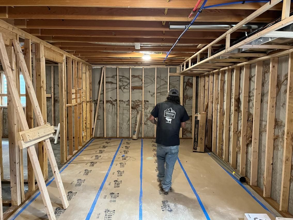 A person walks through a room under construction, framed with wood, marked with blue tape.