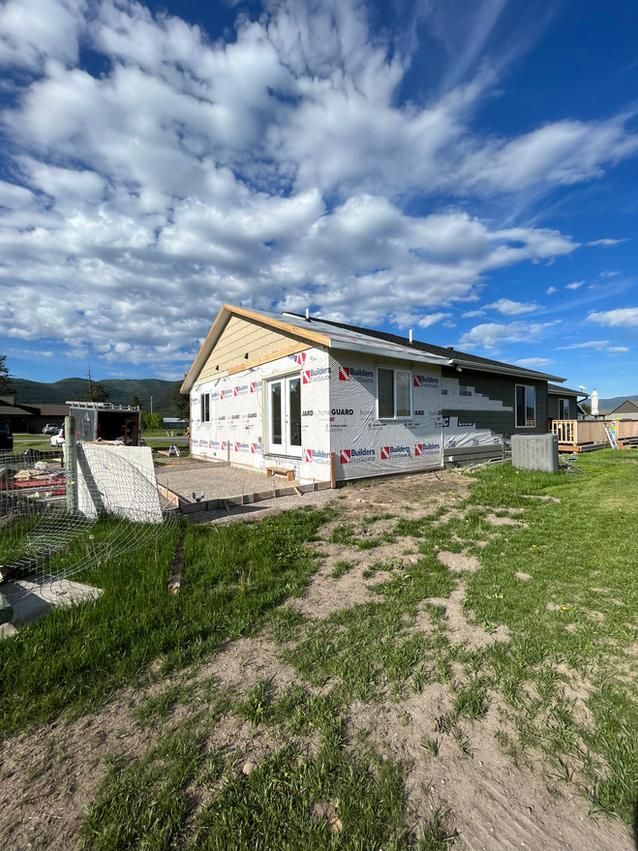 House under construction with exposed siding, surrounded by grass and a cloudy sky.