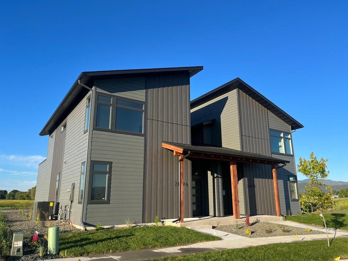 Modern two-story house with dark gray siding, wooden accents, and a covered entrance on a sunny day.