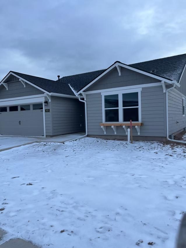 Gray house with a snow-covered yard. Window with a wooden planter. Cloudy sky overhead.