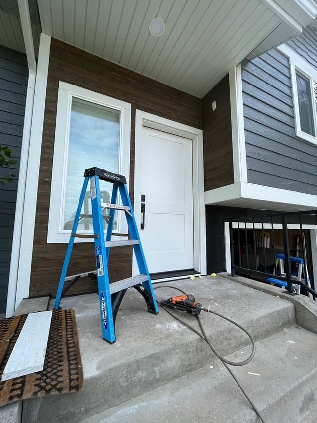 A blue ladder sits in front of a white door, with a saw and step on a concrete porch.