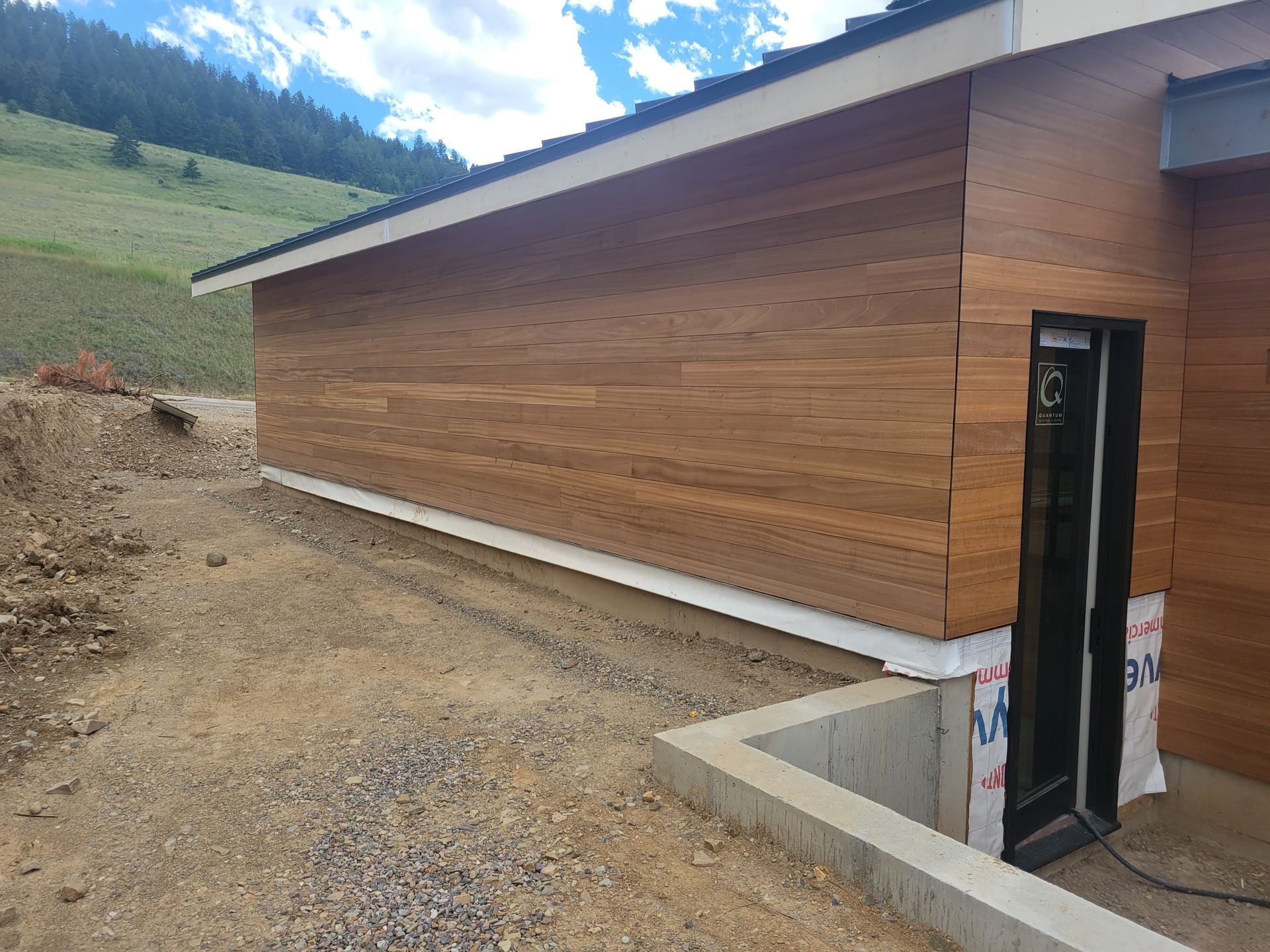 A house with a wooden siding and a black door is sitting on top of a dirt hill.