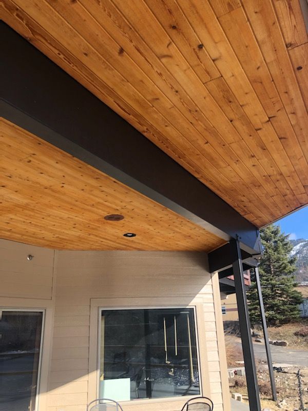 Wooden ceiling with dark beams, part of a building's exterior. Windows and a mountain in the background.