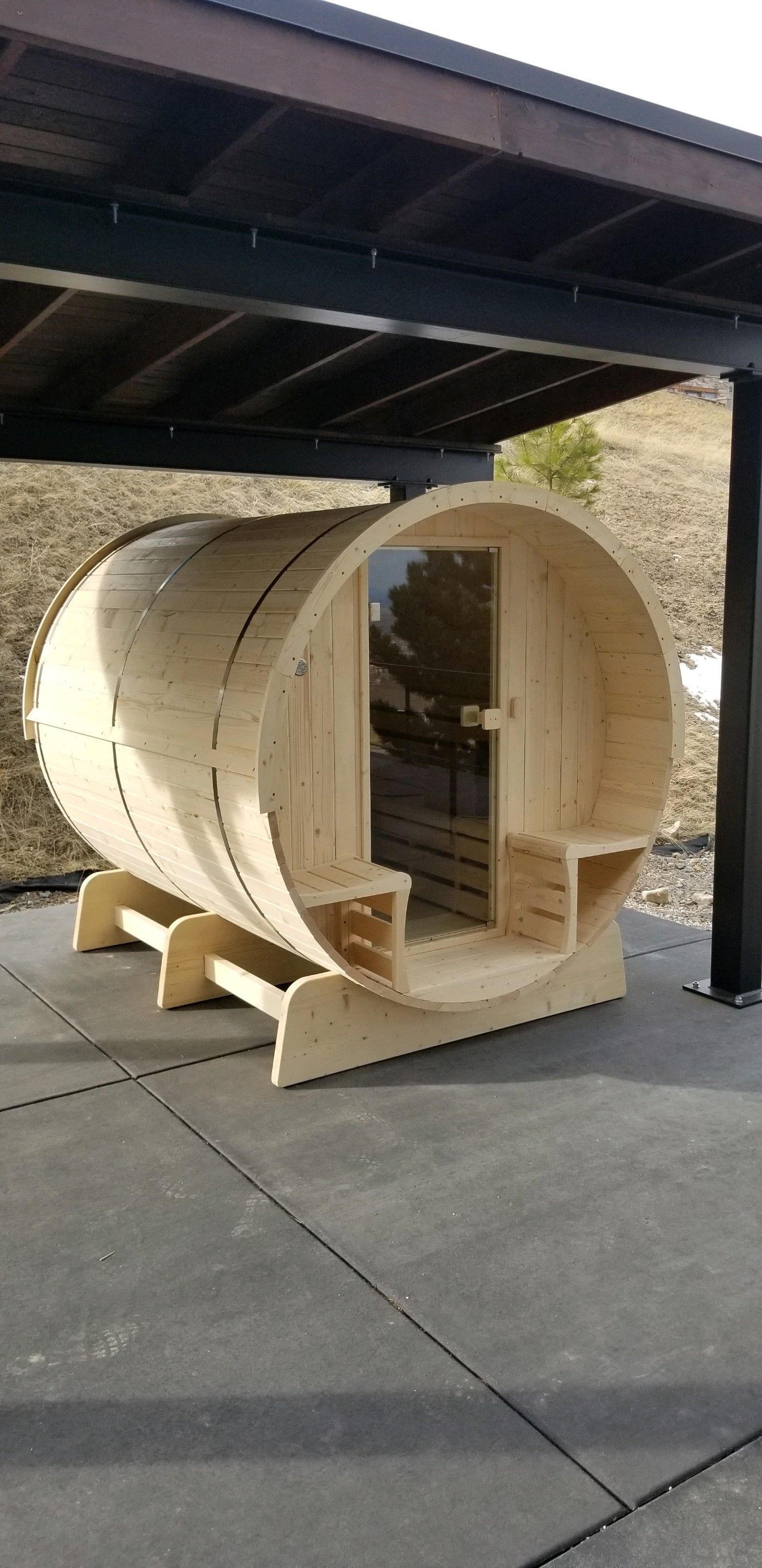 A wooden barrel is sitting under a carport.